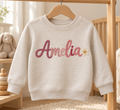 Natural Heather personalized toddler sweatshirt with Amelia sample name and daisy. Flat printed embroidery effect; illustrative mockup.